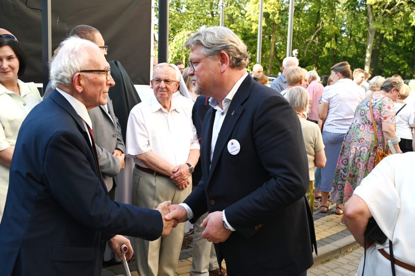 Starszy mężczyzna w garniturze wita się uściskiem dłoni z mężczyzną w garniturze podczas spotkania jubileuszowego Bonifratrów