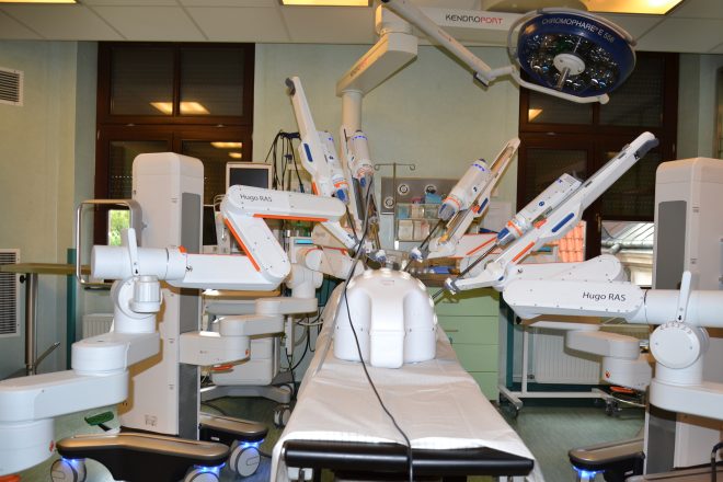 Widok sali operacyjnej z zamontowanym robotem chirurgicznym Hugo RAS firmy Medtronic – w centralnej części widoczne wieloramienne ramię robota ustawione nad stołem operacyjnym, przygotowane do ćwiczeń lub zabiegu