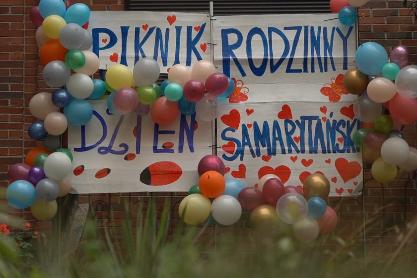 Baner pikniku – Ręcznie malowany napis „Piknik Rodzinny – Dzień Samarytański” ozdobiony balonami w wielu kolorach
