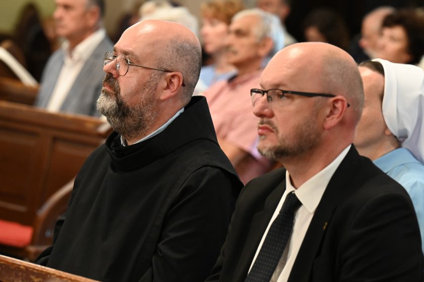 Zakonnik i mężczyzna w garniturze siedzą obok siebie w kościele, skupieni na liturgii jubileuszowej