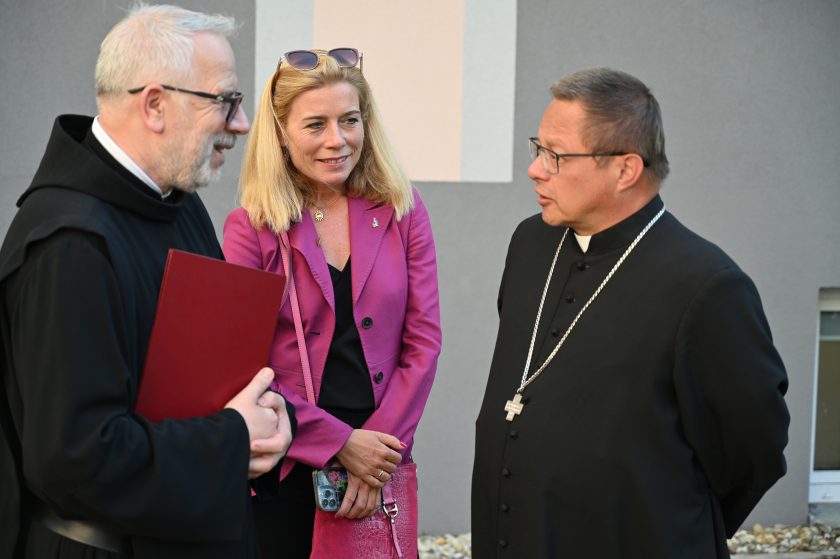 Zakonnik rozmawia z kobietą w różowej marynarce i księdzem w czarnej sutannie z pektorałem
