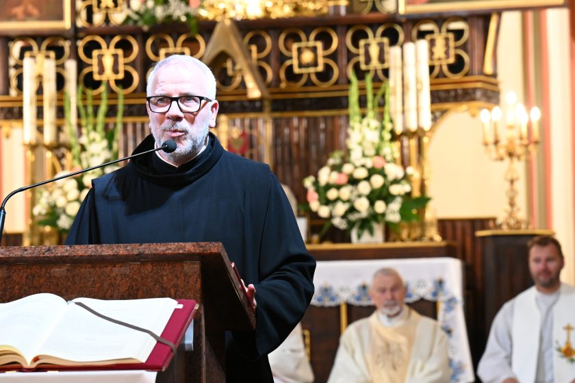 Zakonnik w habicie wygłasza kazanie przy ambonie, w tle ołtarz ozdobiony kwiatami i świecami
