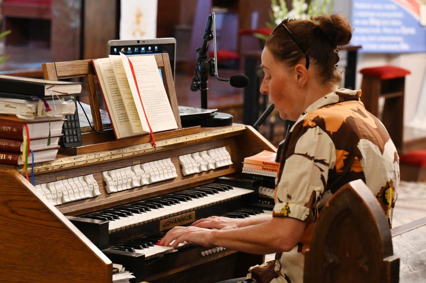 Kobieta grająca na organach podczas liturgii, przed nią otwarta księga i nuty ułożone na pulpicie instrumentu