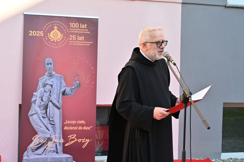 Zakonnik odczytuje przemówienie przy mikrofonie, stojąc obok baneru jubileuszowego Zakonu Bonifratrów