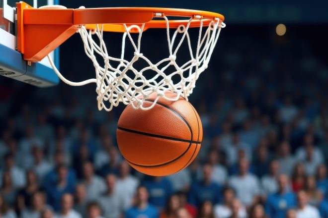 Piłka do koszykówki wpadająca do obręczy z siatką podczas meczu w hali sportowej, na tle widowni pełnej kibiców