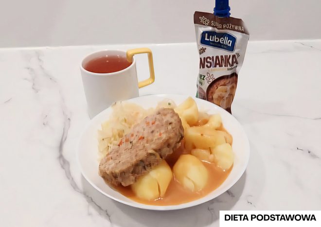 Na talerzu obiadowym w ramach „Diety podstawowej” znajdują się ziemniaki, kotlet mielony w sosie oraz surówka z kapusty. Do zestawu podano kubek herbaty oraz deser – owsiankę kakaową w saszetce