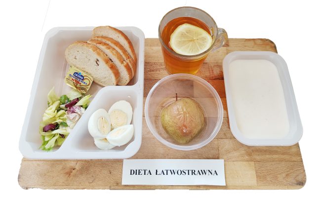 Taca ze śniadaniem w diecie łatwostrawnej: jajko na twardo w plasterkach i mieszanka sałat w jednym pojemniku, obok kilka kromek chleba pszennego, porcja masła, gotowana gruszka w oddzielnym naczyniu, herbata z plasterkiem cytryny oraz miseczka z białym kleikiem lub kaszką mleczną