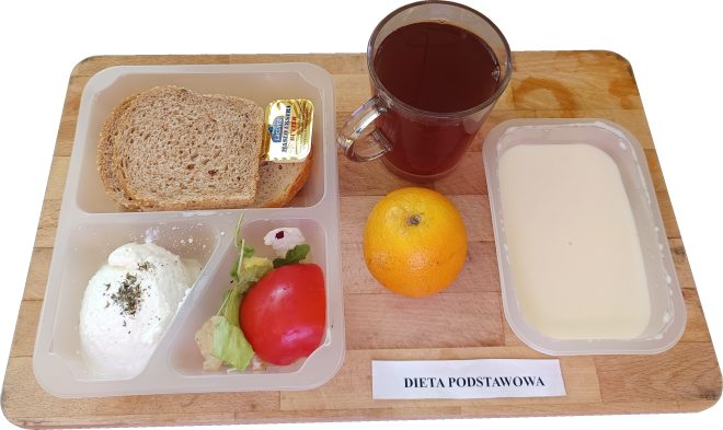 Śniadanie obejmujące pieczywo pełnoziarniste z porcją masła, twaróg posypany ziołami, plaster pomidora z listkiem sałaty, pomarańczę, kubek herbaty oraz porcję białego jogurtu lub mlecznego deseru. Posiłek skomponowany w ramach diety podstawowej