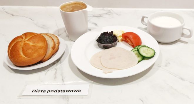 Śniadanie – dieta podstawowa: Bułka kajzerka i kromki chleba pszennego, dwa plasterki wędliny drobiowej, pomidor, ogórek, porcja masła, konfitura z czarnej porzeczki, kawa z mlekiem i kubek mleka