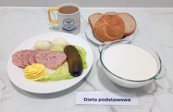 Taca ze śniadaniem w diecie podstawowej: talerz z trzema plastrami kiełbasy, połówkami jajka na twardo, sałatą, ogórkiem kiszonym i porcją masła; obok bułka i kromki chleba pszennego, kubek kawy z mlekiem oraz miseczka z białym napojem mlecznym