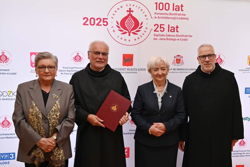 Cztery osoby stoją na tle ścianki z logotypami jubileuszu 100-lecia Konwentu Bonifratrów w Archidiecezji Łódzkiej i 25-lecia Szpitala św. Jana Bożego w Łodzi.