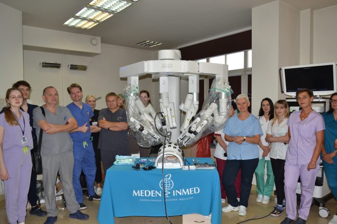 Grupa lekarzy i pielęgniarek stoi wokół robota chirurgicznego podczas prezentacji sprzętu medycznego