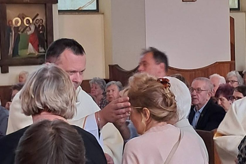 Kapłan w ornacie kładzie dłoń na głowie kobiety podczas udzielania błogosławieństwa, w tle modlący się wierni i obrazy Drogi Krzyżowej