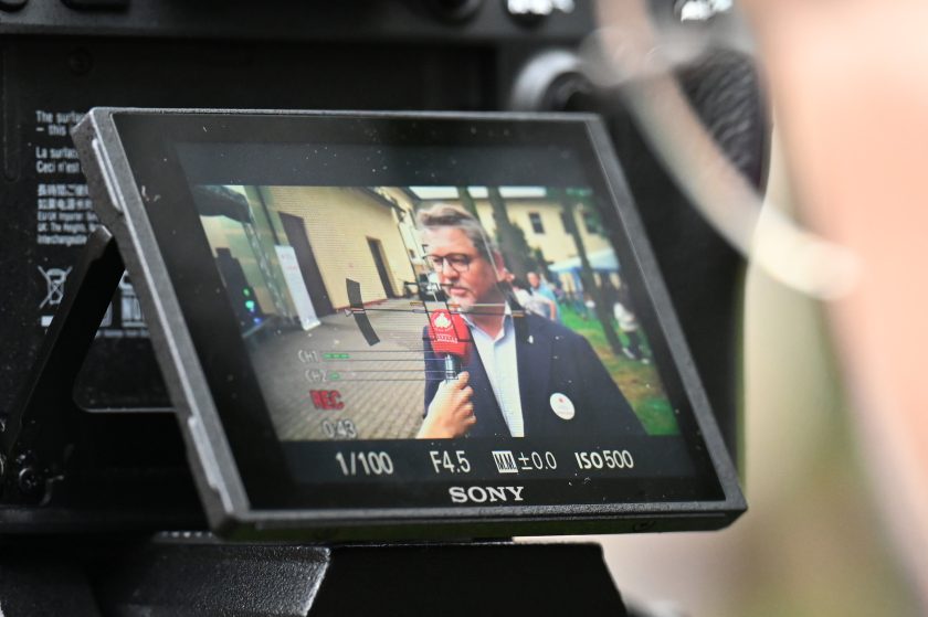 Ujęcie ekranu aparatu fotograficznego pokazujące nagranie wywiadu. Na wyświetlaczu widać mężczyznę w garniturze, który mówi do mikrofonu z logo Fundacji Bonifraterskiej