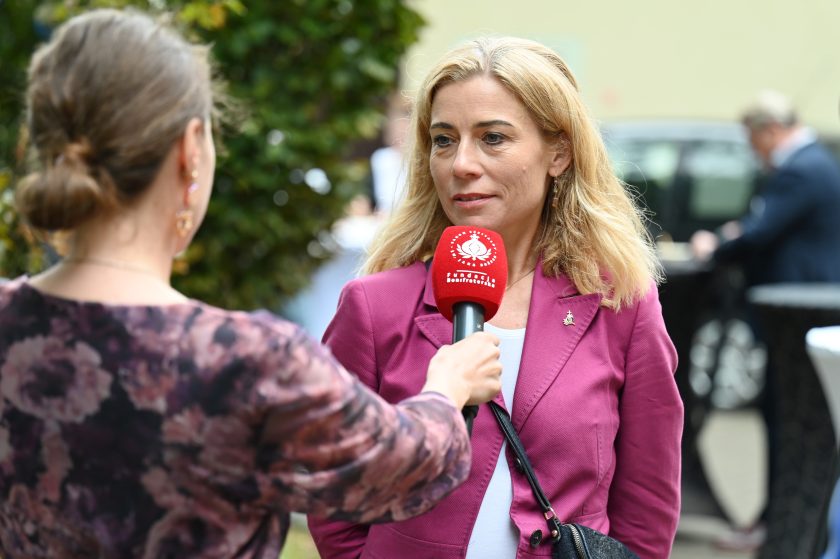 Kobieta w różowym żakiecie udziela wywiadu. Przed nią mikrofon z logo Fundacji Bonifraterskiej, obok widoczna rozmówczyni w kwiecistej bluzce