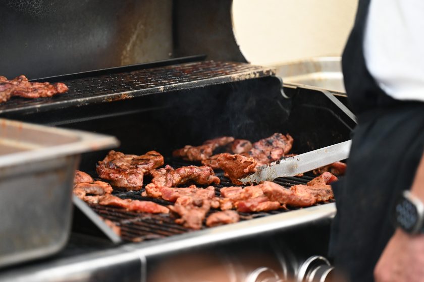 Zbliżenie na grill, na którym pieką się kawałki mięsa. Na ruszcie widać soczyste, rumieniące się porcje