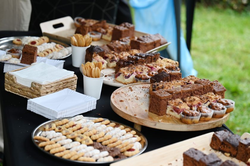 Stół z poczęstunkiem – ciasta, muffiny i ciasteczka ułożone na tacach i półmiskach, obok papierowe serwetki i kubeczki