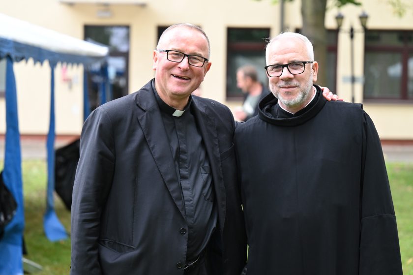 Dwaj duchowni w serdecznej atmosferze – uśmiechnięci ksiądz i brat zakonu bonifratrów pozują razem do zdjęcia, symbolizując współpracę i wspólnotę