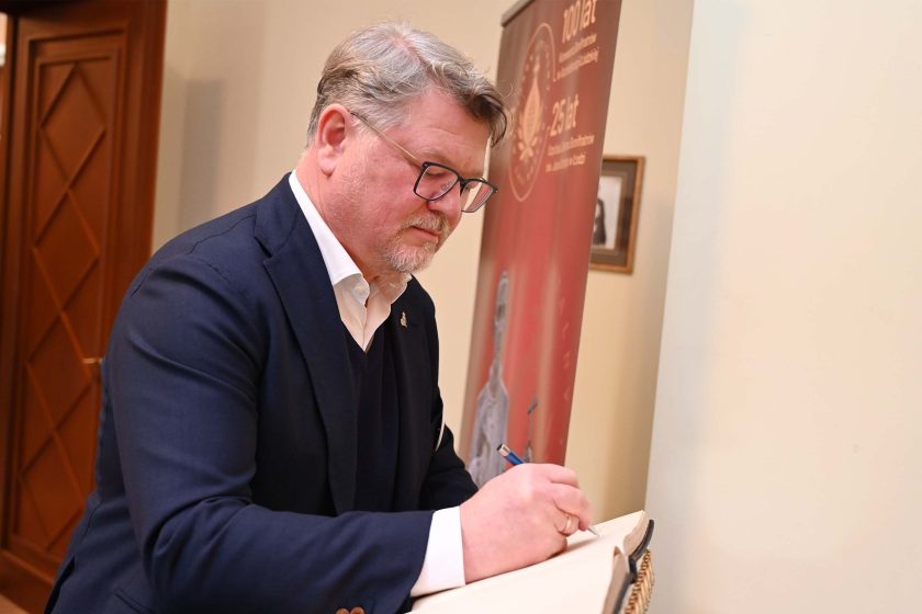 Mężczyzna w marynarce i okularach wpisuje się do księgi pamiątkowej jubileuszu Bonifratrów.