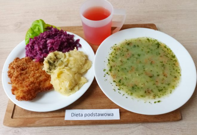 Obiad w diecie podstawowej: kotlet schabowy w panierce, ziemniaki z koperkiem i surówka z czerwonej kapusty. Do tego talerz zupy jarzynowej z natką pietruszki i kubek z kompotem