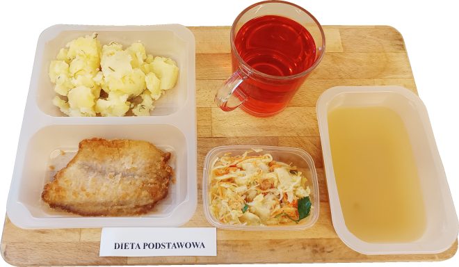 Obiad w diecie podstawowej: porcje ziemniaków z koperkiem, panierowany filet rybny oraz surówka z kapusty i marchewki w oddzielnym pojemniczku. Do zestawu dołączona zupa jarzynowa w miseczce i szklanka czerwonego kompotu