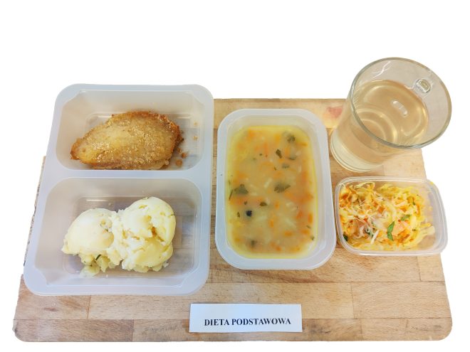 Na tacy podano zestaw obiadowy w wersji diety podstawowej. W menu znajduje się zupa jarzynowa z kawałkami warzyw, panierowany kotlet podany z porcją puree ziemniaczanego, surówka z kapusty białej z marchewką oraz napój w szklance. Posiłek skomponowany jest w sposób zbilansowany – łączy źródło białka, węglowodanów i witamin