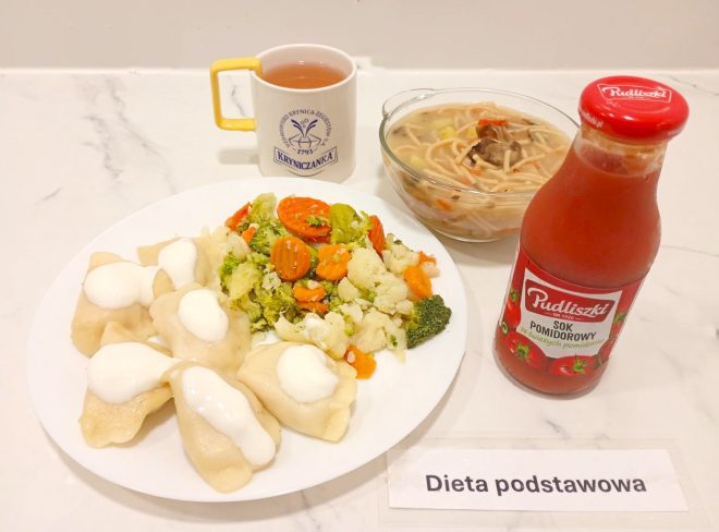 Zestaw obiadowy w diecie podstawowej: pierogi polane śmietaną, gotowane warzywa (marchew, brokuł, kalafior), zupa z makaronem, herbata w kubku „Kryniczanka” oraz sok pomidorowy w butelce Pudliszki