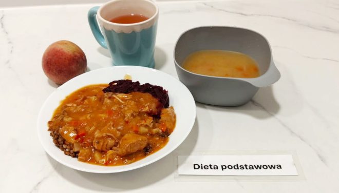 Obiad w ramach diety podstawowej. Na talerzu podano kaszę gryczaną z sosem i kawałkami duszonego mięsa w warzywach, a obok porcję buraczków. W miseczce znajduje się lekka zupa jarzynowa. Do zestawu dołączono brzoskwinię oraz kubek z herbatą.
