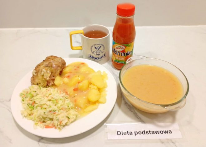 Zestaw obiadowy w diecie podstawowej: zupa jarzynowa w misce, ziemniaki z sosem, pieczony kawałek mięsa, surówka z kapusty, kubek herbaty i butelka soku owocowego