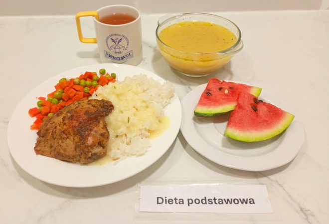 Obiad w diecie podstawowej: pieczone udko kurczaka, ryż z sosem, marchewka z groszkiem, kawałki arbuza, zupa w misce oraz kubek herbaty