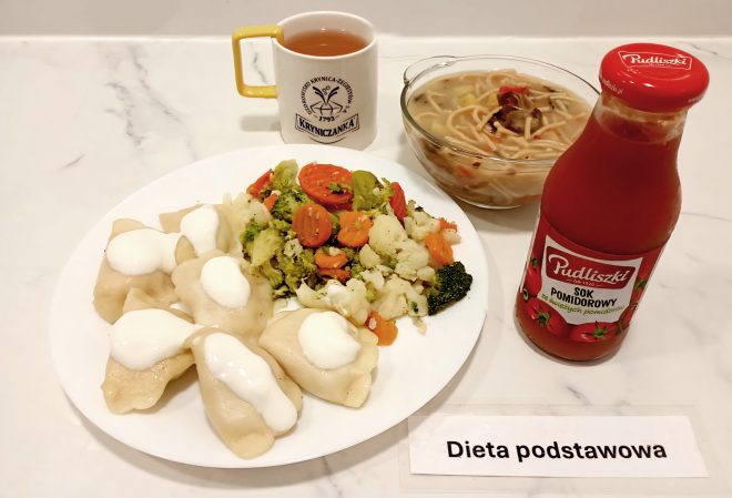 Zestaw obiadowy w diecie podstawowej: pierogi polane śmietaną, gotowane warzywa (brokuł, marchew, kalafior), zupa z makaronem, szklanka herbaty w kubku „Kryniczanka” oraz sok pomidorowy w butelce