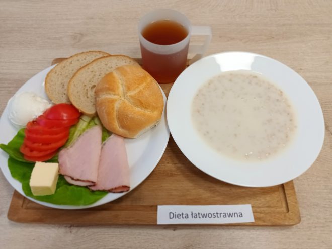 Śniadanie: pieczywo jasne i bułka, plasterki szynki, ser żółty, pomidor i sałata z masłem, miseczka płatków owsianych na mleku oraz kubek herbaty