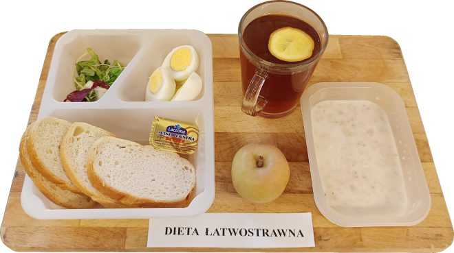 Śniadanie w diecie łatwostrawnej: kromki białego pieczywa z porcją masła, jajko gotowane na twardo, sałata, jabłko. Obok owsianka mleczna w pojemniczku i herbata z cytryną w szklance