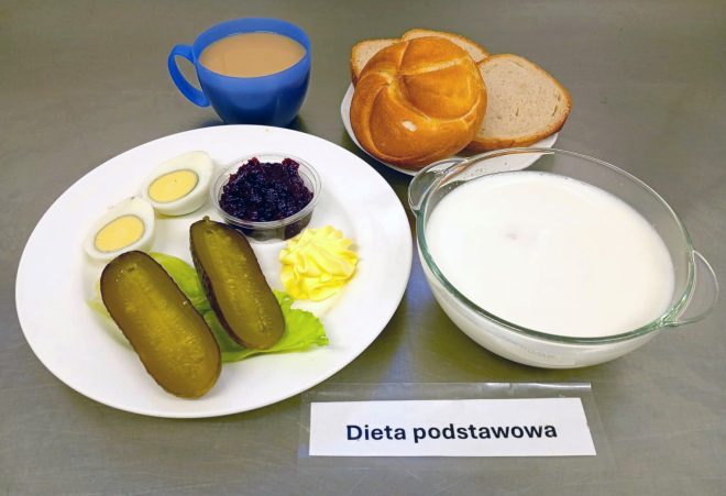 Śniadanie w diecie podstawowej: jajko gotowane na twardo, ogórek kiszony, porcja konfitury owocowej, masło, bułka i kromki chleba pszennego, kubek kawy z mlekiem oraz miska zupy mlecznej