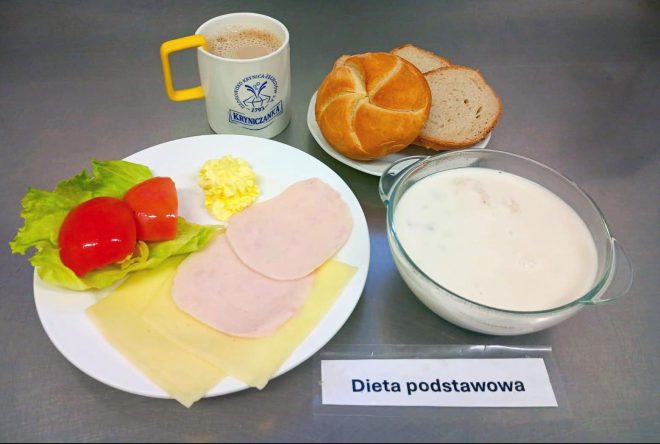 Śniadanie w diecie podstawowej: bułka i kromki chleba, plasterki sera żółtego i wędliny drobiowej, pomidor z sałatą, masło, zupa mleczna w miseczce oraz kubek kawy z mlekiem