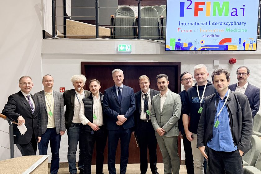 Uczestnicy forum I²FIM ai edition stoją wspólnie w rzędzie przed salą konferencyjną. W tle widać ekran z kolorowym logo wydarzenia „International Interdisciplinary Forum of Innovative Medicine”.