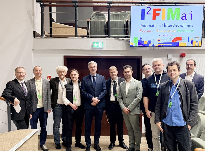 Uczestnicy forum I²FIM ai edition stoją wspólnie w rzędzie przed salą konferencyjną. W tle widać ekran z kolorowym logo wydarzenia „International Interdisciplinary Forum of Innovative Medicine”.
