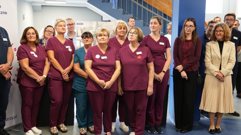 Grupa pielęgniarek w bordowych uniformach stoi na tle niebieskiej klatki schodowej, rozmawiając i uśmiechając się podczas spotkania w Bonifraterskim Centrum Medycznym