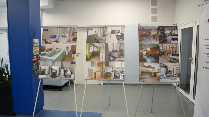 Wnętrze placówki z wystawą plansz prezentujących zdjęcia pomieszczeń przed i po remoncie. Na tablicach widać fotografie sal rehabilitacyjnych, gabinetów oraz zaplecza medycznego z podpisami „Tak było” i „Tak jest”