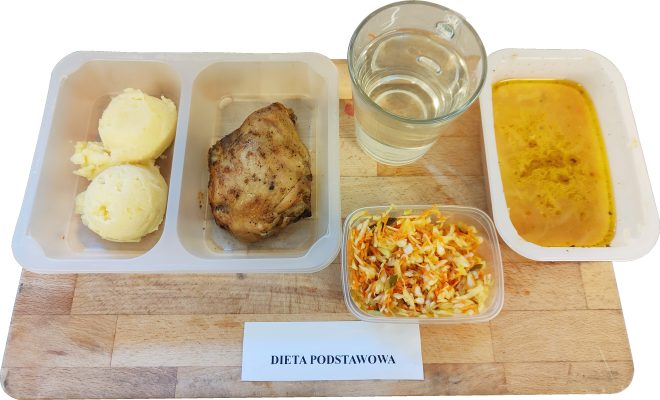 Posiłek w diecie podstawowej – zbilansowany i pełnowartościowy. Na talerzu porcja ziemniaków, duszone mięso drobiowe, surówka z kapusty i marchwi oraz aromatyczna zupa warzywna. Do picia woda. To przykład tradycyjnego, domowego obiadu serwowanego w ramach codziennego żywienia pacjentów