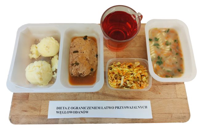 Taca z obiadem w diecie z ograniczeniem łatwo przyswajalnych węglowodanów. W zestawie znajdują się puree ziemniaczane, kotlet mielony w sosie, surówka z kapusty i marchewki, zupa jarzynowa z makaronem oraz kubek czerwonego napoju owocowego