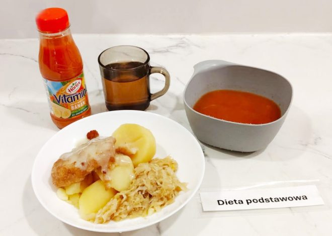 Zestaw obiadowy w diecie podstawowej. Na talerzu ziemniaki z sosem, panierowany kotlet i kapusta zasmażana. Obok miska z zupą pomidorową, szklanka herbaty i butelka soku Hortex Vitaminka. Na stole kartka z napisem „Dieta podstawowa”