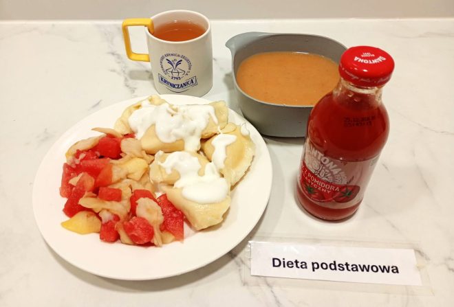 Obiad w diecie podstawowej: pierogi z serem polane śmietaną, podane z kompotem owocowym i surówką z jabłka oraz arbuza. W zestawie także zupa pomidorowa i sok pomidorowy. To pełnowartościowy, domowy posiłek, łączący tradycyjny smak i prostotę przygotowania