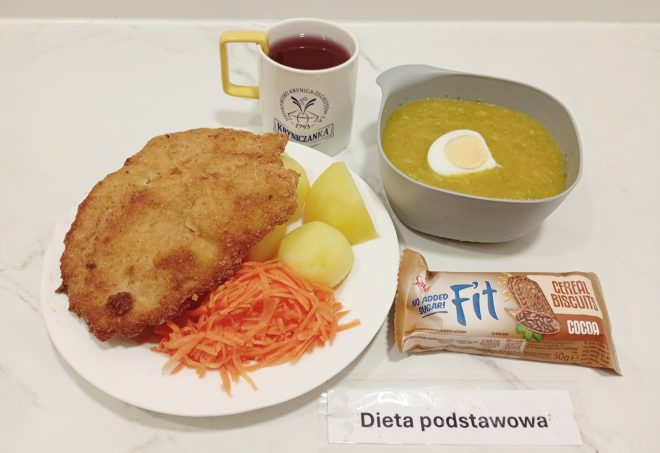 Obiad w diecie podstawowej: kotlet schabowy z gotowanymi ziemniakami i surówką z marchwi, zupa krem z groszku z połówką jajka na twardo, kubek z herbatą oraz batonik zbożowy Fit