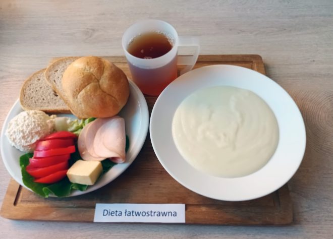 Lekkie śniadanie w diecie łatwostrawnej: pieczywo pszenne i żytnie, wędlina drobiowa, ser twarogowy, masło, pomidor i sałata. Do tego filiżanka delikatnej herbaty oraz kremowa zupa mleczna. Posiłek dostarcza energii i jest odpowiedni dla osób z wrażliwym układem pokarmowym