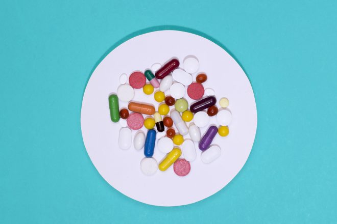 Różnokolorowe tabletki i kapsułki rozsypane na białym, okrągłym krążku na turkusowym tle