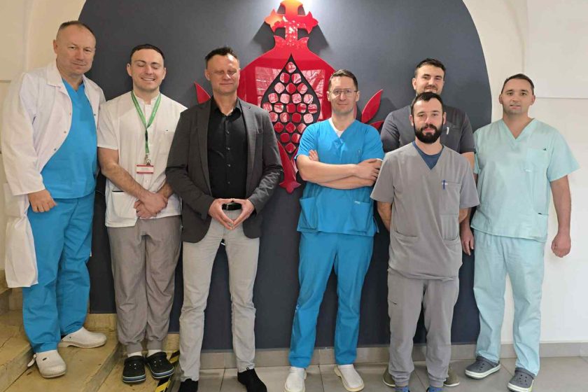 Zespół medyczny i przedstawiciele szpitala podczas wspólnej fotografii wykonanej w jednym z pomieszczeń placówki. Wszyscy ustawieni przed symbolem nawiązującym do tradycji bonifraterskiej