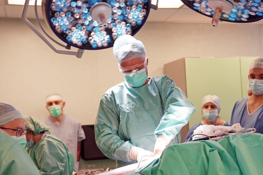 Zespół chirurgów podczas trwającego zabiegu w sali operacyjnej. Personel skoncentrowany na pracy wykonuje precyzyjne czynności w sterylnych warunkach, przy świetle lamp operacyjnych