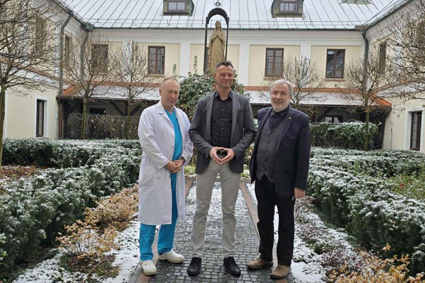 Spotkanie na dziedzińcu przyklasztornym, w otoczeniu zimowej scenerii. Na zdjęciu przedstawiciele szpitala oraz zaproszony gość, w tle widoczne charakterystyczne zabudowania kompleksu