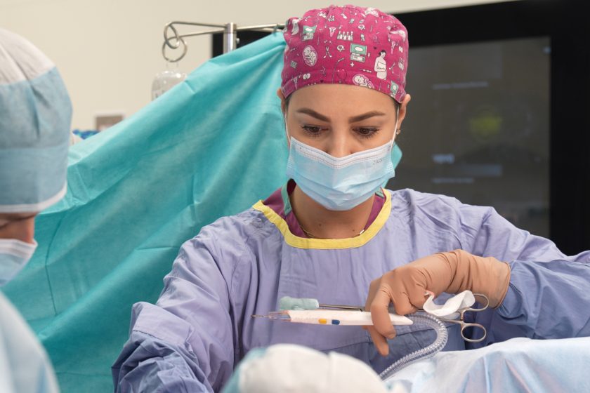 Lekarka w czepku z kolorowym wzorem i maseczce operacyjnej wykonuje precyzyjne czynności podczas operacji, trzymając narzędzia chirurgiczne